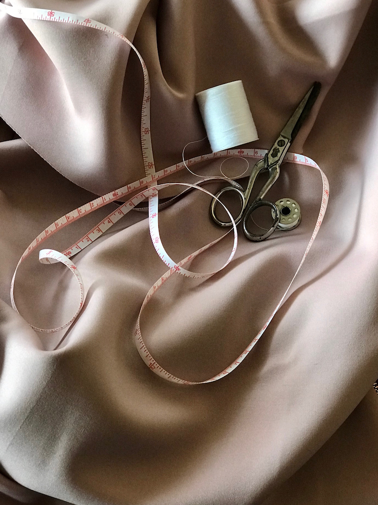 Paire de ciseaux, bobine de fil blanc et mètre ruban posés sur du tissu rose poudré